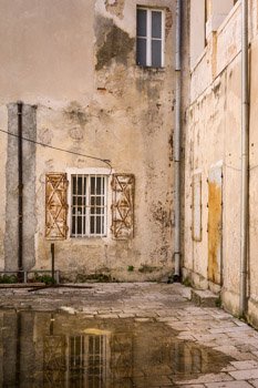 Old buildings surround a decaying courtyard in the heart of Zadar, Croatia. A window framed by iron bars is reflected in a puddle of rainwater. Prints available in any size, on any material. For more information, please click the Purchase link above.