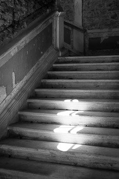 "Slip Sliding Away" Black and White Fine Art Photograph Made by Nat Coalson. In an old, decaying stairwell, deep within a centuries-old building in the heart of Zadar, Croatia, the narrow daylight from a circular window illuminates a small spot on a few steps. Black and white photograph. Prints available; for details click the Purchase link above.