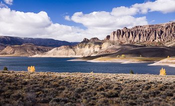 Puffy, white clouds glide over the parched landscape, creating dramatic shadows on the massive, eroded sandstone cliffs at Blue Mesa Reservoir near Gunnison, Colorado. Prints available; for details click the Purchase link above.